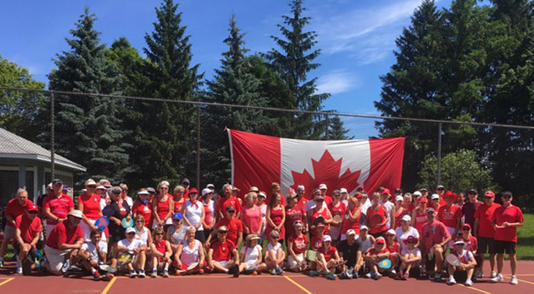 Members in red and white in front of a large Canadian flag on the courts, Canada Day 2019