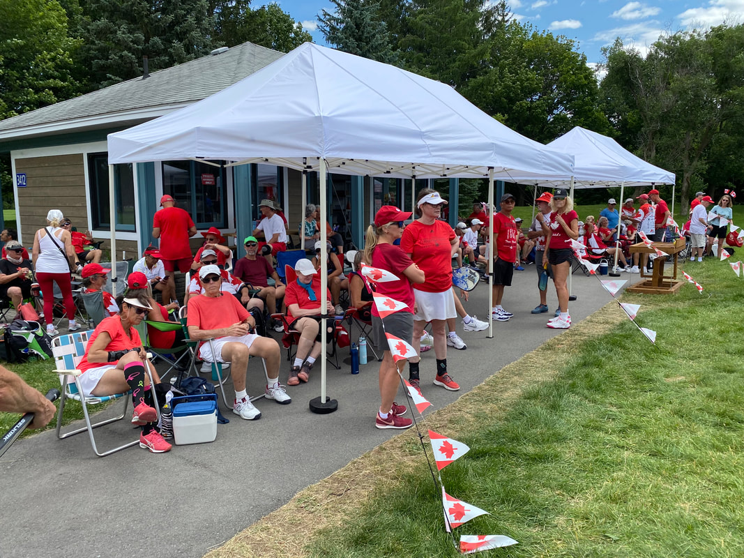 Members in red and white under the tents beside the courts